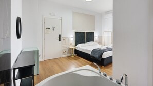 Ein modernes Hotelzimmer mit einem großen Bett, einem eigenen Badezimmer inklusive Badewanne und einem kleinen Nachttisch.