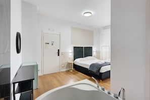 Habitació d'hotel moderna amb un llit gran, un bany separat amb banyera i una petita taula de nit.