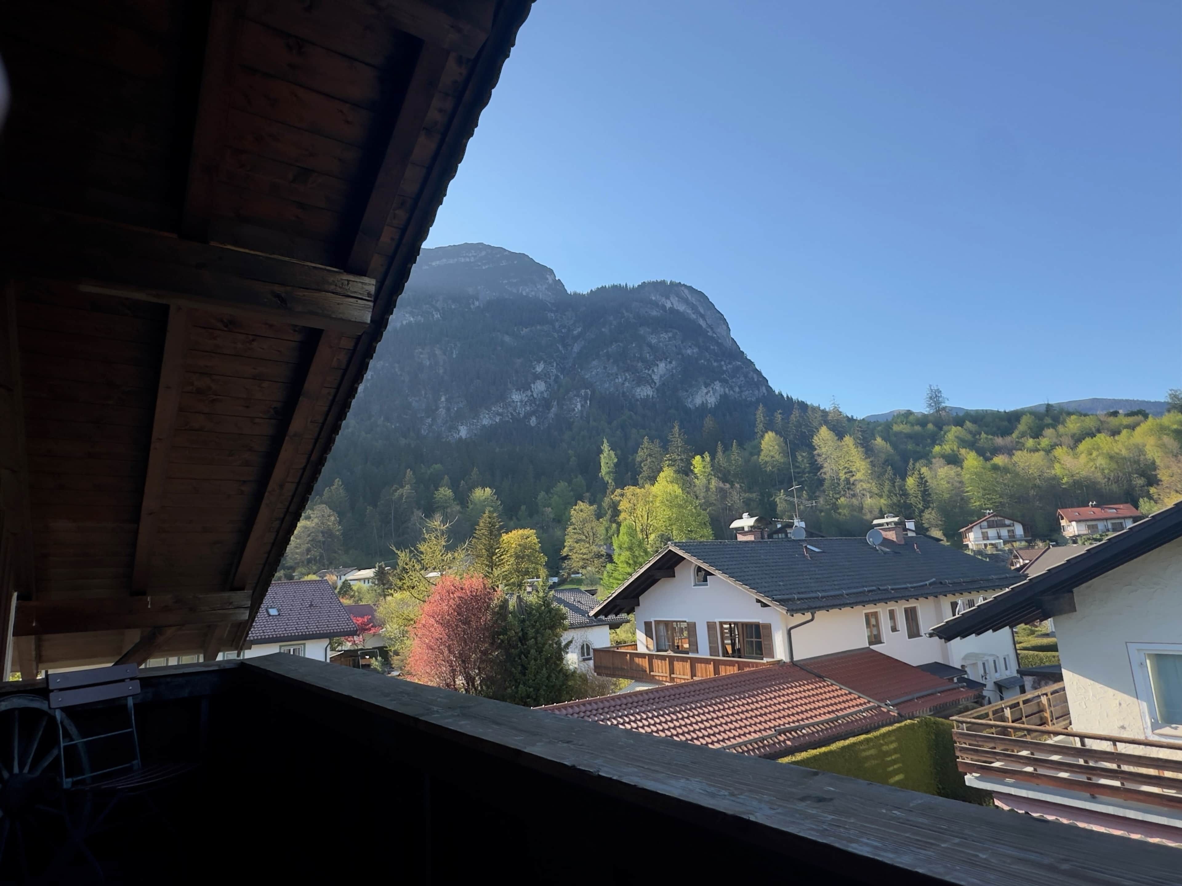 Bergblick von einem Holzhaus mit sichtbaren Häusern und blauem Himmel.