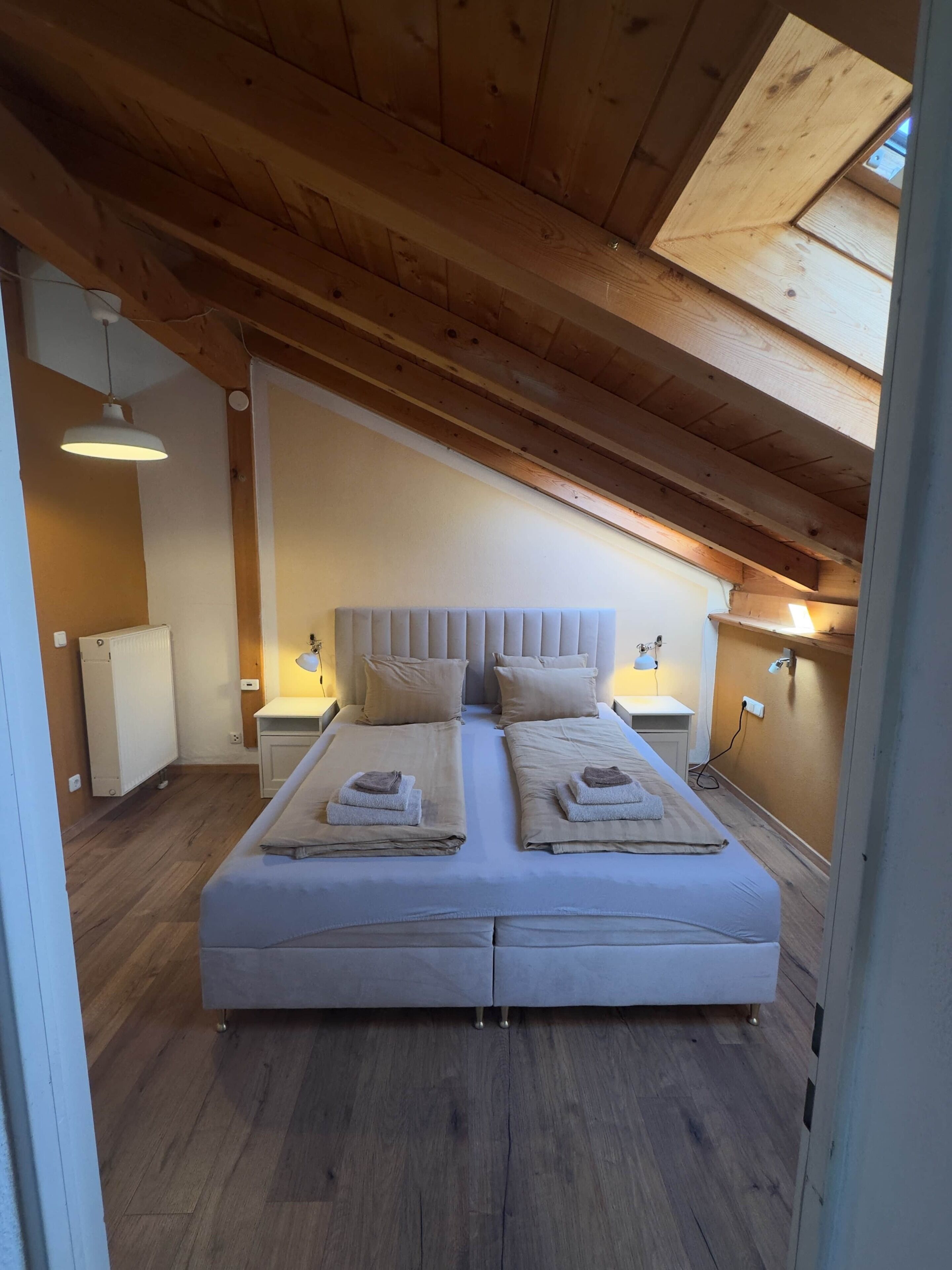 Ein Schlafzimmer mit einem großen Bett, Holzbalkendecke, Nachttischlampen und einer Heizung.