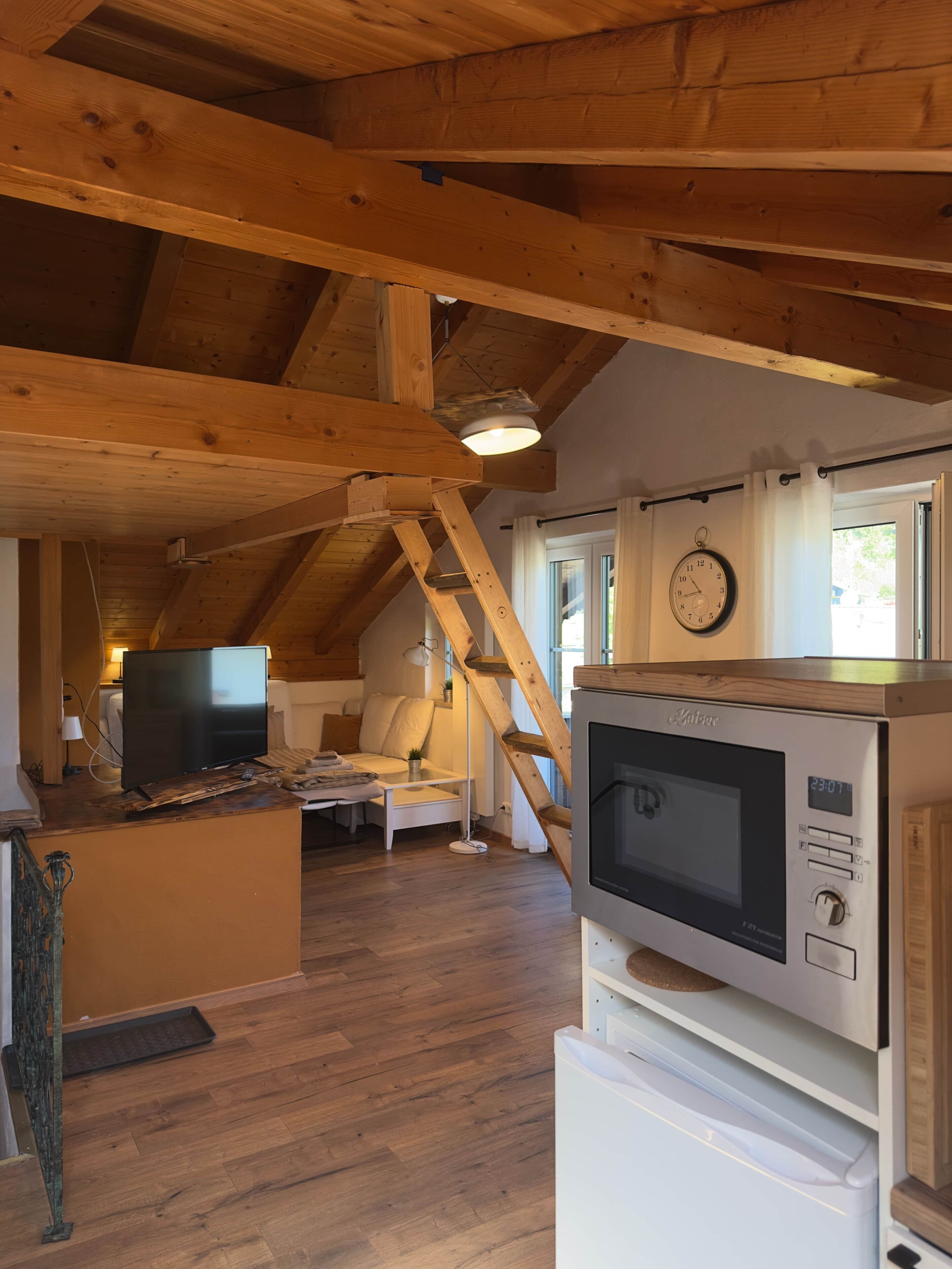 Interior em madeira com televisão, micro-ondas e relógio na parede.