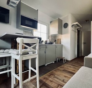 A compact kitchen with a microwave, cabinets, and a small stool. - Apartment-Wohnung 2 Mountain View (Garmisch-Partenkirchen)