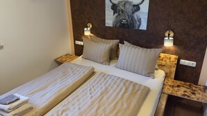 Una cama doble con dos almohadas, una lámpara de pared e imagen enmarco de un toro.