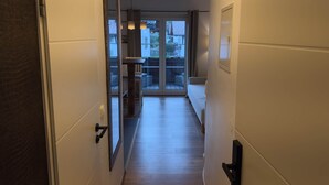 Un pasillo que conduce a un balcón con una mesa y sillas, una puerta con manija y vistas a edificios.
