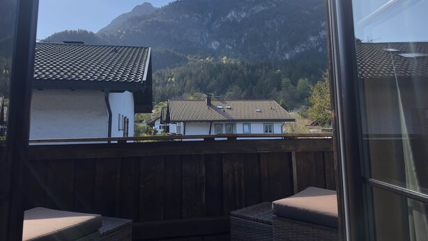 Un balcón con vista a una montaña, una cerca de madera y un edificio con tejado de tejas.