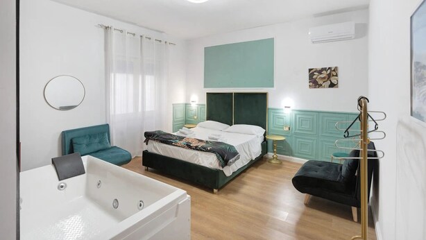 Ein Schlafzimmer mit einem Bett, einem Sessel, einem kleinen Tisch, einem Kleiderständer und einer Badewanne.