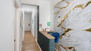 A reception area with a marble wall, a wooden reception desk, a blue chair, and a hallway leading to a door. - Mirosa Luxury Room 214 with Wi-Fi and Air Conditioning (Pompei)