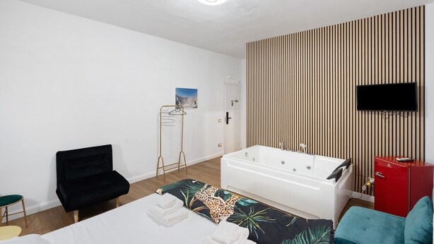 A modern hotel room with a bed, a black chair, a red cabinet, a wooden slat wall, a white bathtub, and a flat-screen TV. - Mirosa Luxury Room 214 with Wi-Fi and Air Conditioning (Pompei)