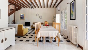 Un coin repas avec une table dressée pour quatre personnes, des chaises en bois, une nappe blanche, un radiateur et un escalier menant à une autre pièce.