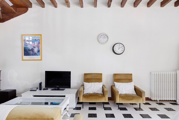 A modern living room with a flat-screen TV, two armchairs, a coffee table, and a framed picture on the wall.