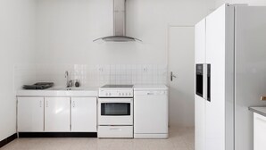 Une cuisine compacte avec des meubles blancs, un four encastré, un lave-vaisselle et une hotte de cuisinière en acier inoxydable.