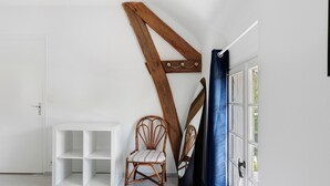 Une pièce avec une porte blanche, une étagère blanche, une chaise en osier et une guitare appuyée contre le mur.