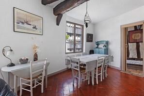 Ein Essbereich mit einem weißen Tisch und Stühlen, einem Fenster mit Vorhängen, einer Hängelampe und einem gerahmten Bild an der Wand.