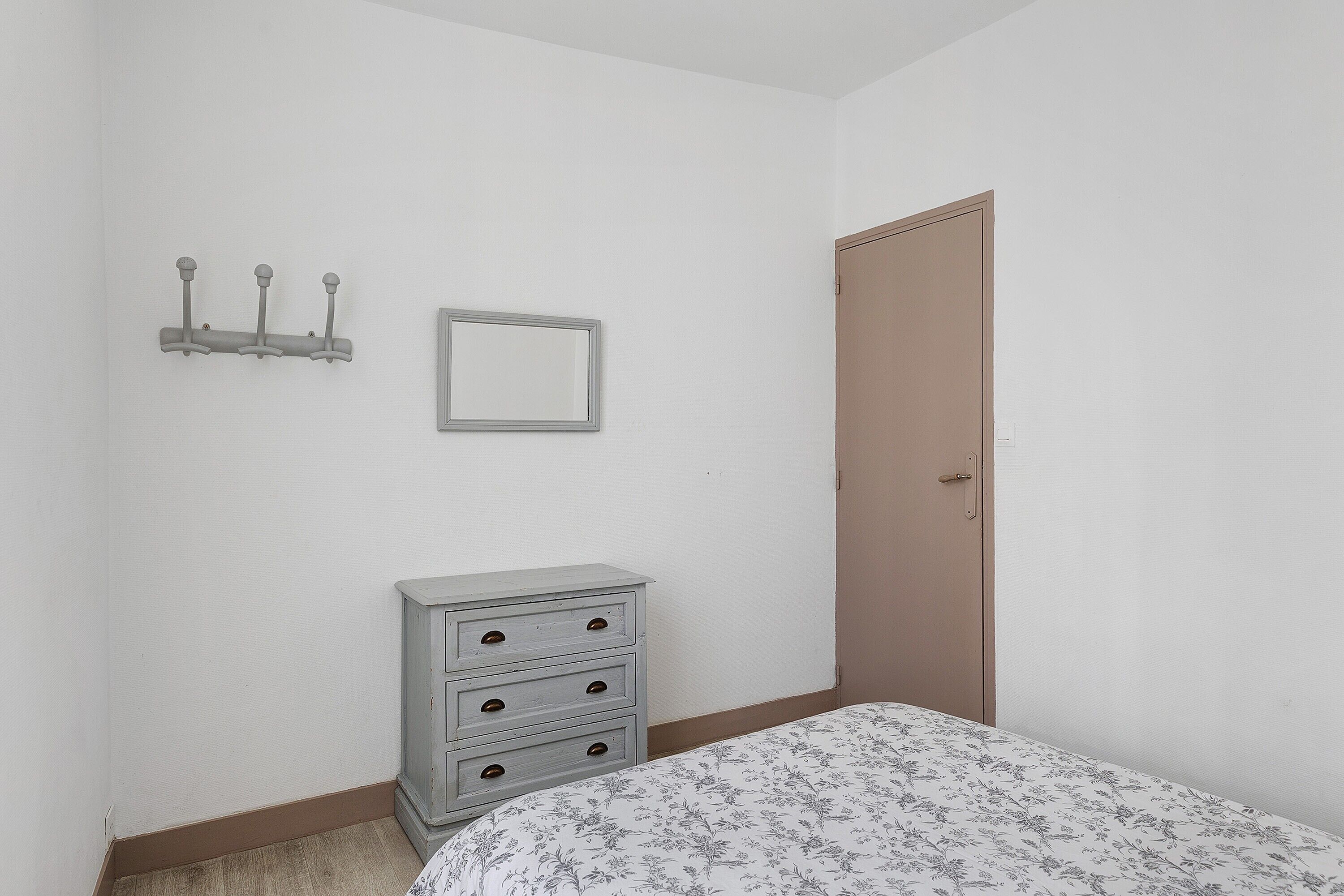 A bedroom with a bed, a dresser, a door, a coat rack, and a framed picture on the wall.