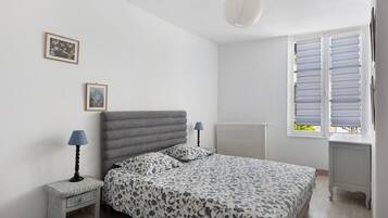 A bedroom with a bed, bedside tables, a radiator, and a window with shutters.