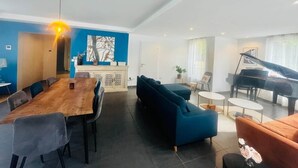 A modern living room with a dining area, a blue sofa, a piano, and a large wooden table. - Villa Exclusive 10pers, Garages, 10 min Cathedral (Strasbourg)
