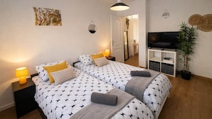 Ett dubbelrum med två sängar, sänglampor, en TV, en växt och konstverk på väggarna.
