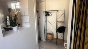 En hall med ett kaklat golv, en vävd matta, ett metallställ med en korg och en krukväxt.