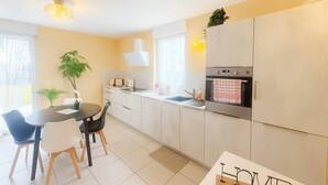 A modern kitchen with white cabinets, a black countertop, and a built-in oven. There is a dining table with chairs and a potted plant. - Nid des Étoiles, garden, 5 min Strasbourg (Oberhausbergen)