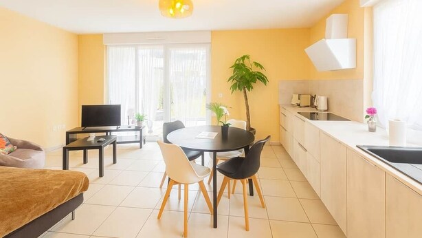 A modern living room with a sofa, TV, dining table, chairs, and a kitchen area with a sink and cabinets. - Nid des Étoiles, garden, 5 min Strasbourg (Oberhausbergen)