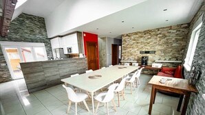 A modern kitchen with a stone wall backsplash, a dining area with a long table and white chairs, and a small seating area with a red sofa. - Villa with indoor pool (Holtzheim)