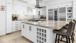 A modern kitchen with white cabinetry, a central island with bar stools, stainless steel appliances, and a tiled backsplash. - LUX 2BR Pool 5mins Beach | Villa Ocean by Bocobay (Noord)