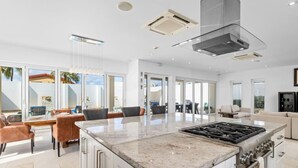 A modern kitchen with a central island, built-in oven, and a large window overlooking a patio area. - LUX 2BR Pool 5mins Beach | Villa Ocean by Bocobay (Noord)