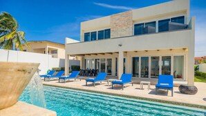 A modern two-story building with a pool area featuring blue lounge chairs and a stone accent. - LUX 2BR Pool 5mins Beach | Villa Ocean by Bocobay (Noord)