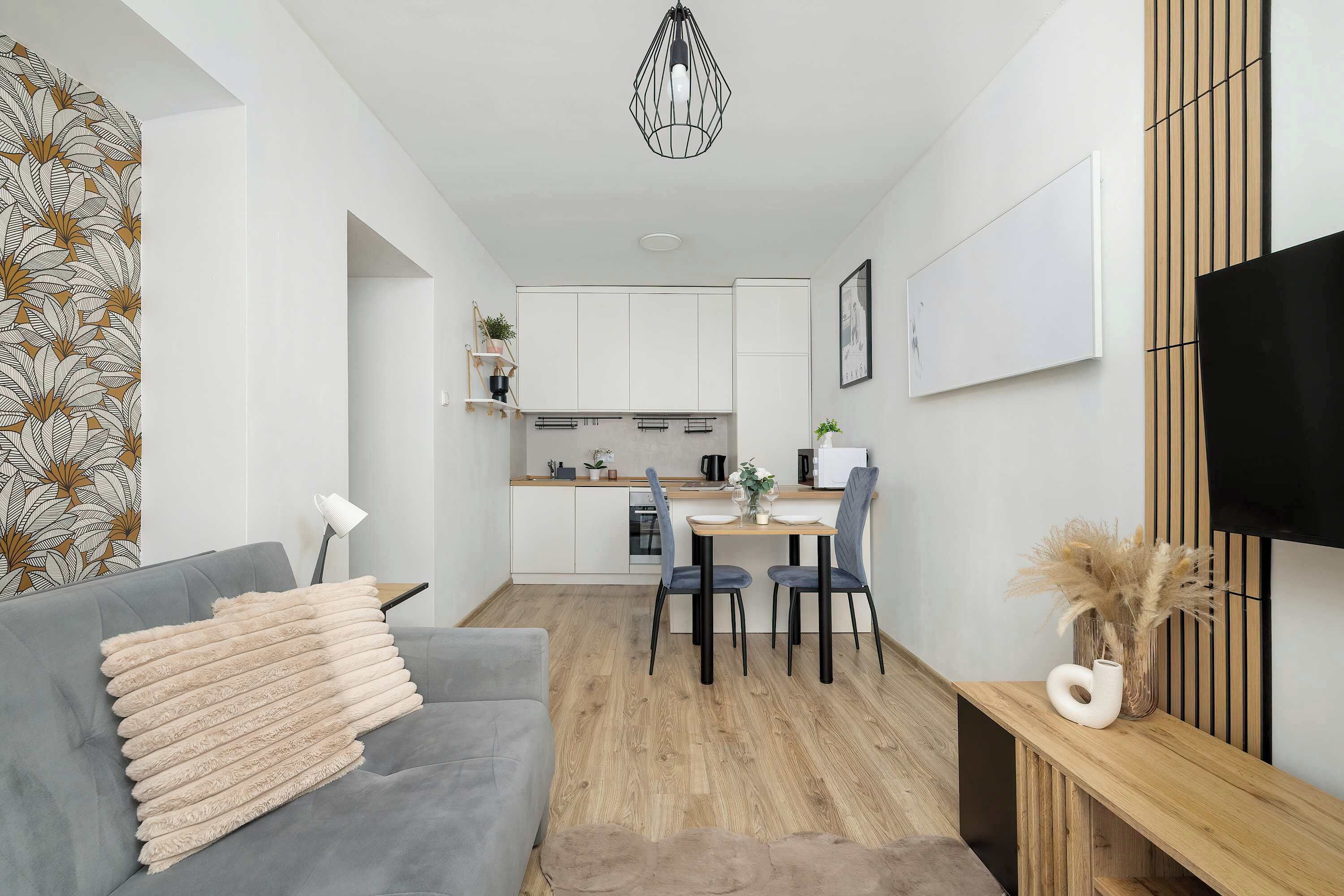 A modern living room with a grey sofa, a wooden dining table, and a kitchen in the background.