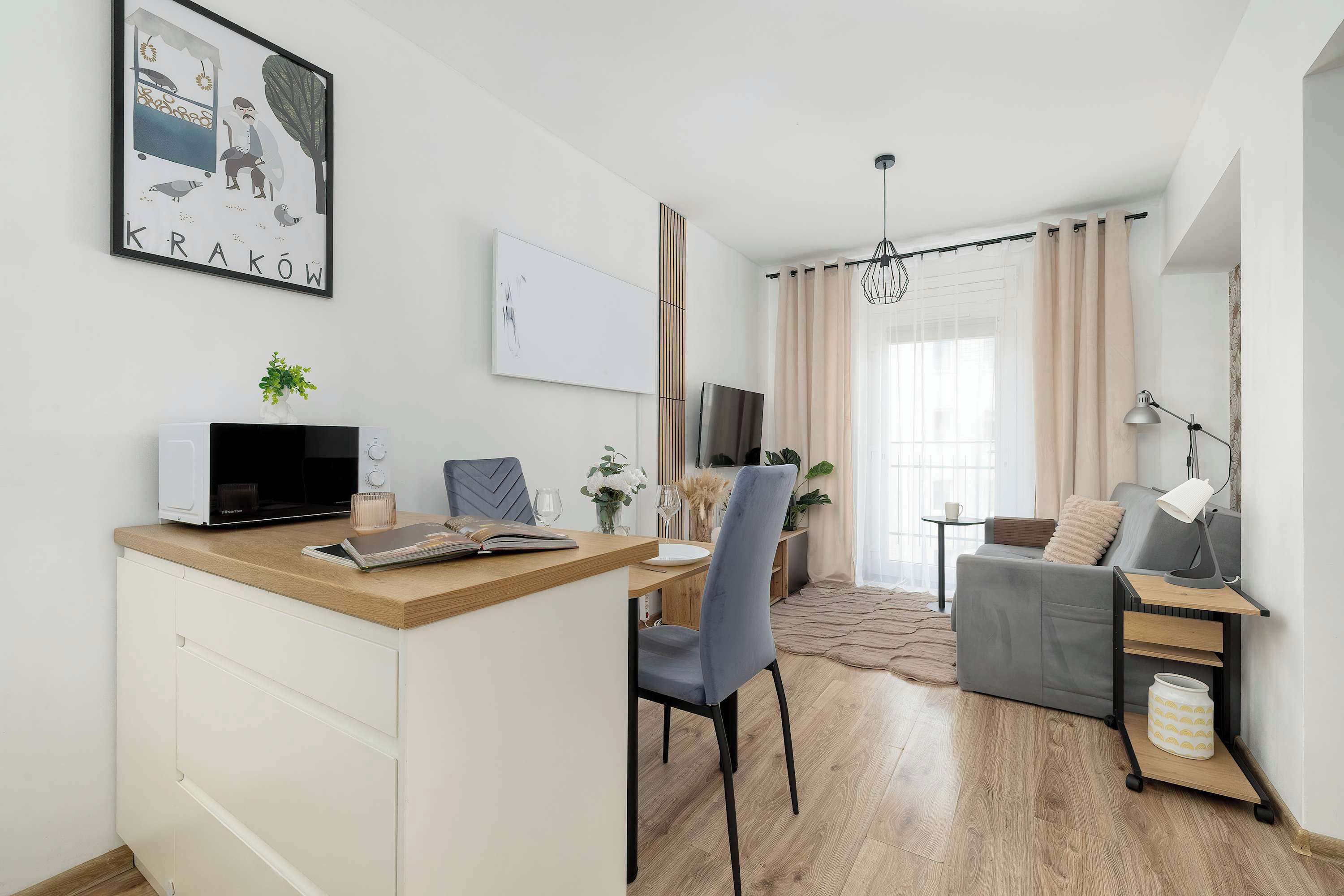 Een moderne woonkamer met een bank, een eethoek met tafel en stoelen, een televisie en een keuken met een magnetron en een plant.