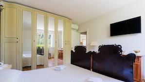 A bedroom with a large bed, a wardrobe, a television, and a bathroom visible through a door. - Holiday Home 'Tenuta Lu Mimmu' with Private Terrace, Wi-Fi and Air Conditioning (Matino)