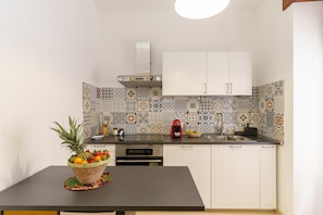A kitchen with white cabinets, a tiled backsplash, a fruit bowl on the counter, and a coffee maker.