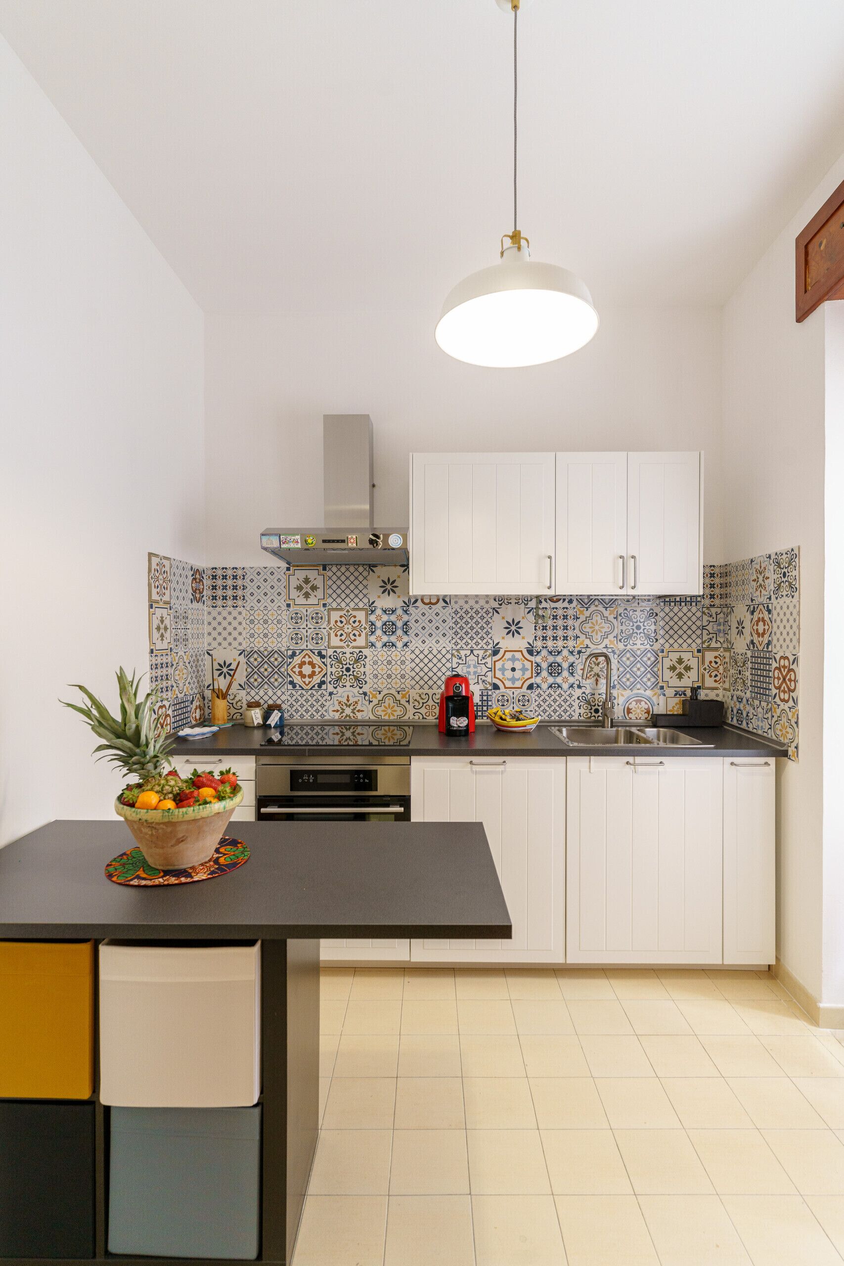 A kitchen with white cabinets, a tiled backsplash, and a fruit bowl on the counter.