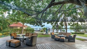 Eine Terrasse im Freien mit Korbmöbeln, einem Tisch und Blick auf ein Gewässer.