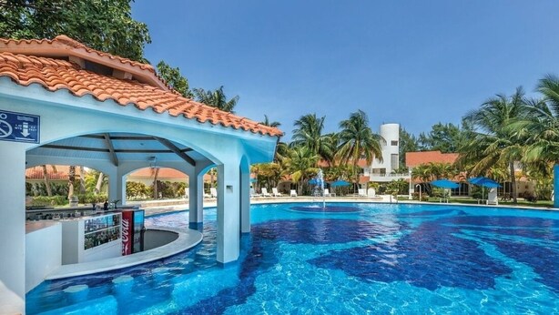 Ein Swimmingpool mit Bar, Palmen und blauem Himmel.
