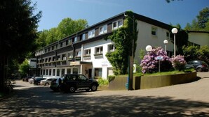 A multi-story hotel with a parking area, a garden with purple flowers, and a clear sky. - Hotel Eifeltor (Mechernich)