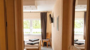 A hotel room with a bed, a chair, a window with curtains, a flat-screen TV, and a mirror. - Hotel Eifeltor (Mechernich)