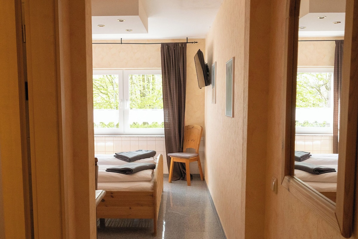 Habitación de hotel con cama, una silla, ventana con cortinas, televisor de pantalla plana y espejo.