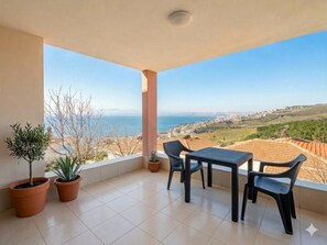 A balcony with a table and chairs, potted plants, and a view of the sea and town. - Quiet and Comfortable in Sinop Karakum Site 3 (Sinop)