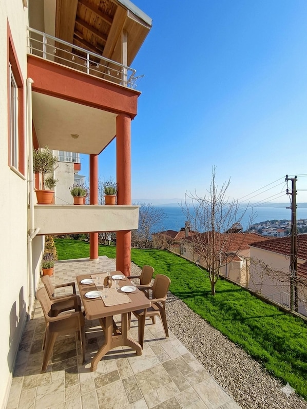 A terrace with a table set for dining, potted plants, and a view of the sea.