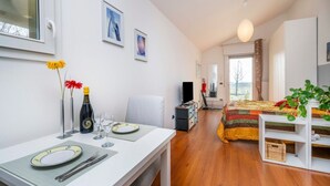 A room with a dining table set, a bed with a colorful bedspread, a television, and a window with curtains. - A comfortable and bright 40 sq m studio apartment, perfect for two people, located on the first floor of a small villa (no elevator).The property is located in an extremely quiet area surrounded by greenery, with a cycle path nearby. Guests can easily re (Udine)