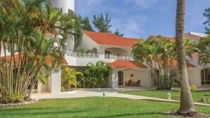 A two-story building with a red-tiled roof, surrounded by palm trees and a well-maintained lawn. - Isla Mujeres | Relaxing Island Retreat | Pool + Beach (Isla Mujeres)