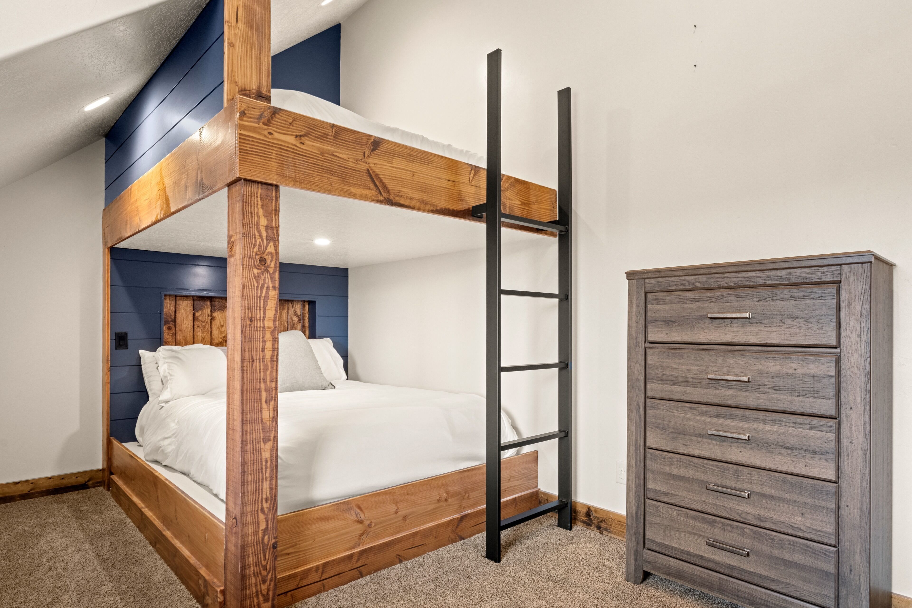A bunk bed with a wooden frame and a ladder, a dresser with drawers, and a blue accent wall.