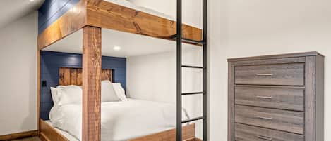 A bunk bed with a wooden frame and a ladder, a dresser with drawers, and a blue accent wall.