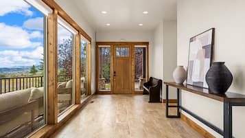A spacious hallway with a view of the outdoors, a wooden bench, a vase, and a framed picture on a console table.