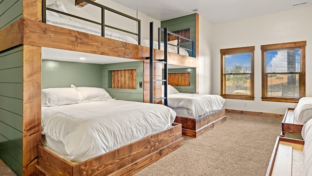 Habitación con literas, una cama alta, una ventana con persianas y piso alfombrado.