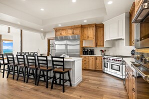 A modern kitchen with wooden cabinets, a stainless steel refrigerator, a built-in oven, and a dining area with wooden chairs.