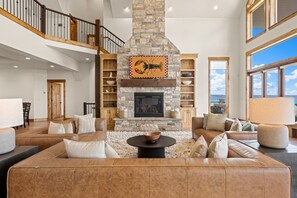 A spacious living room with a stone fireplace, leather sofas, and a high ceiling with skylights.