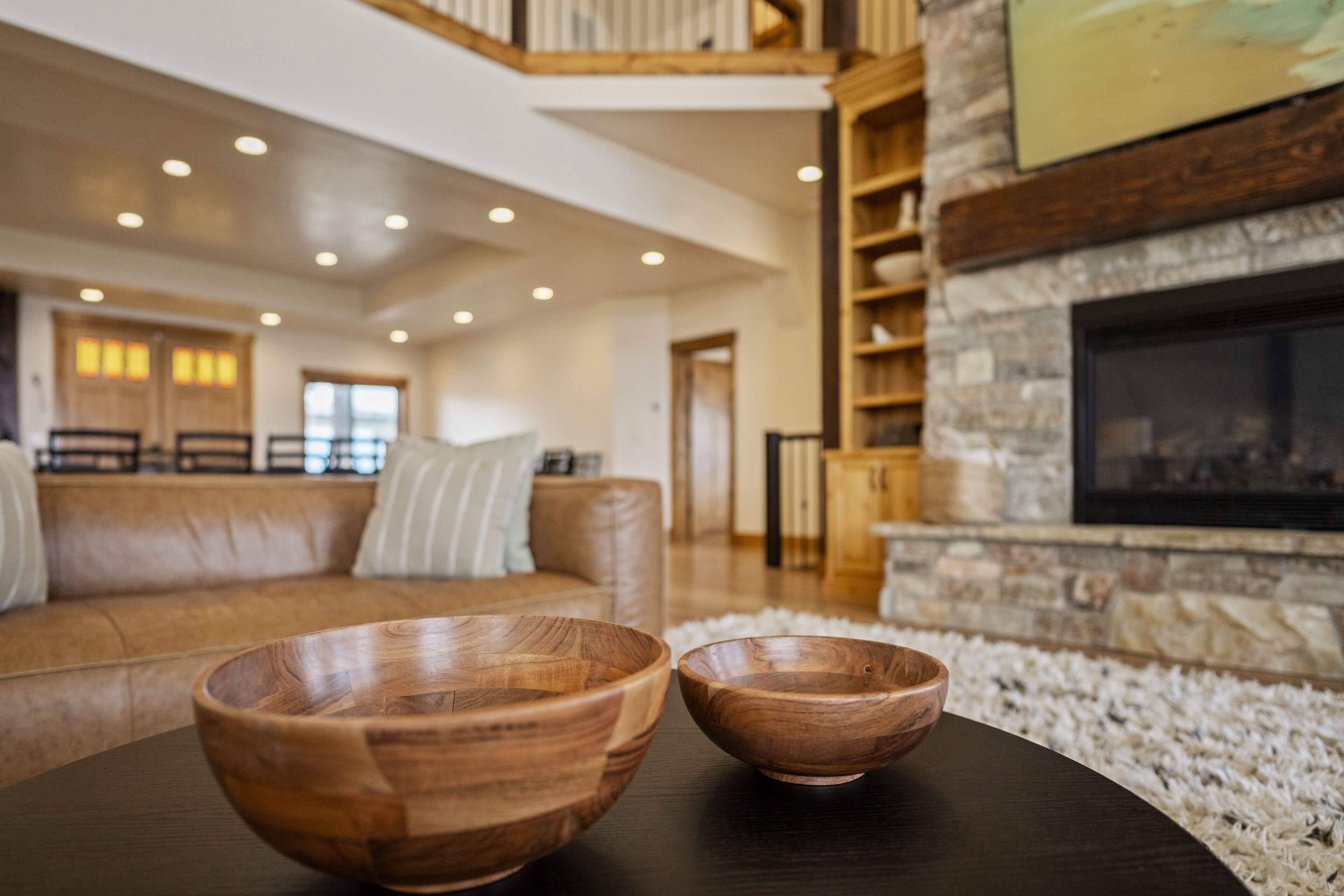 A modern living room with a leather sofa, wooden bowls on a table, and a stone fireplace.