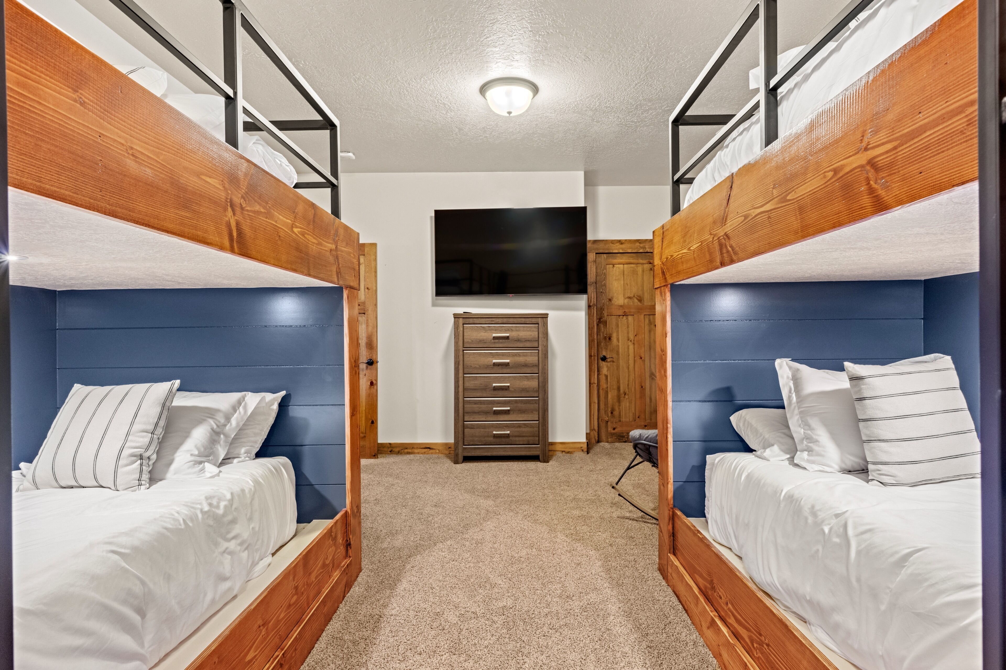 A room with two bunk beds, a flat-screen TV mounted on the wall, and a wooden dresser.